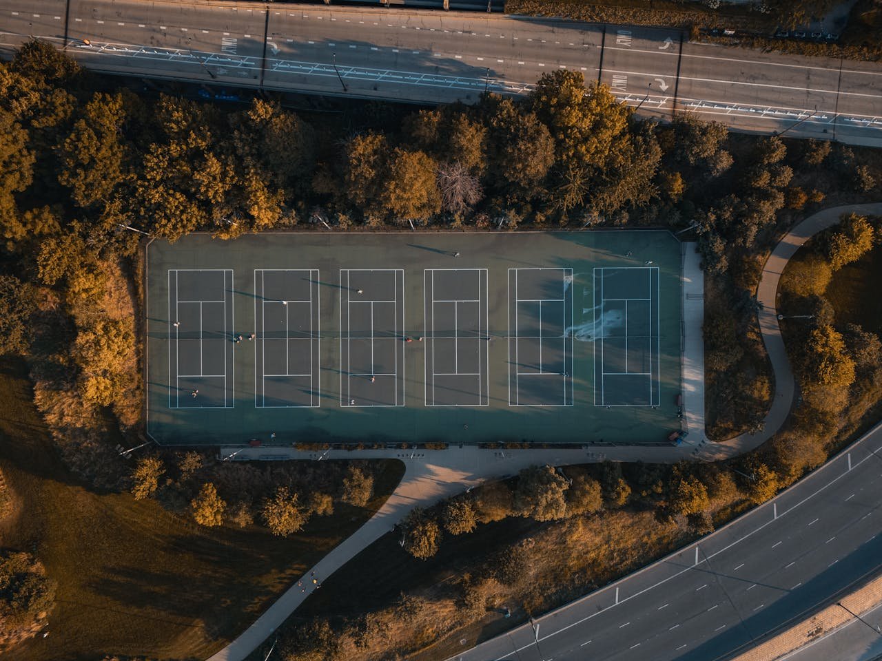 about-03 Aerial shot of tennis courts surrounded by a leafy park and roads.
